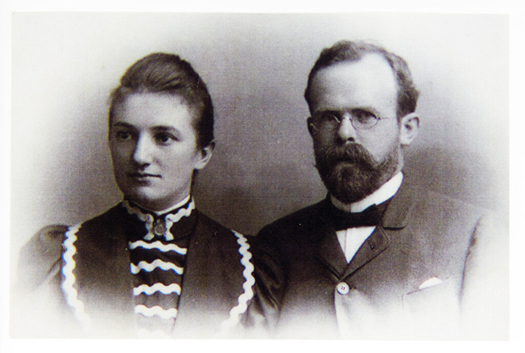 Es ist ein schwarz-weißes Foto. Anna und Otto Snell stehen nebeneinander und sind bis zur Brust abgebildet. Anna Snell ist links und blickt an der Kamera vorbei. Sie trägt ein hochgeschlossenes Kleid mit Paspeln. Otto Snell blickt direkt in die Kamera. Er trägt einen. dunklen Anzug mit Hemd und Fliege. Die Haare sind locker zurückgekämmt und eine Brille mit rundem Metallgestell. Beide sind etwa Mitte dreißig.
