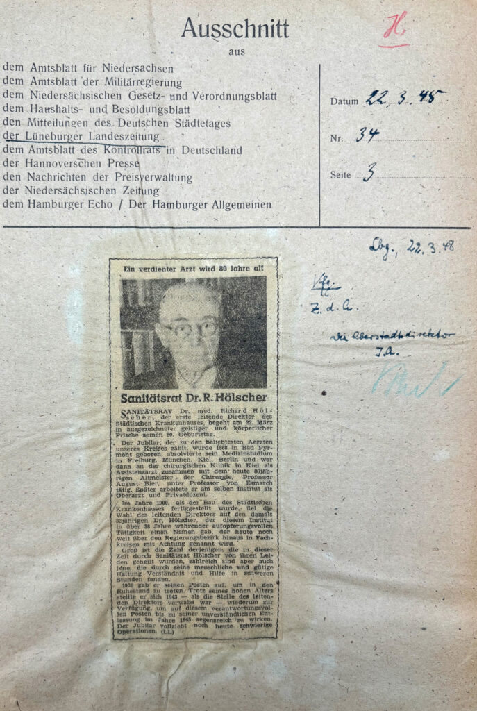 Es ist ein Zeitungsartikel mit einem Porträtfoto des ältlichen Richard Hölscher. Der Artikel ist maschinengetippt und gedruckt auf Zeitungspapier. Er ist einspaltig. Über dem Foto steht: »Ein verdienter Arzt wird 80 Jahre alt«.