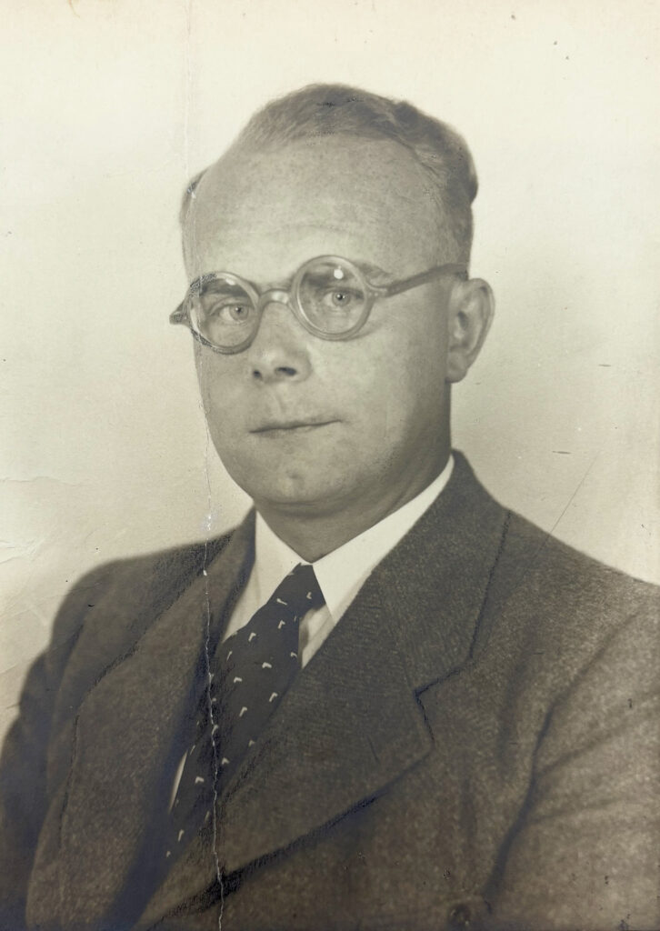 Es ist ein schwarz-weißes Porträt von Werner Kalliske. Er trägt einen dunklen Anzug mit Weste, hellem Hemd und eine gemusterte Krawatte. Er trägt eine Hornbrille. Er hat eine sehr hohe Stirn und ein prägnantes Grübchen am Kinn. Seine kurzen Haare sind nach hinten gekämmt. Er trägt keinen Bart.