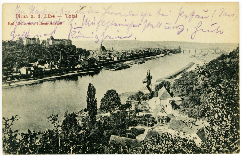 Die Postkarte mit einer schwarz-weißen Stadtansicht ist leicht vergilbt. Es ist ein erhöhter Blick auf den Lauf des Flusses Elbe zu sehen. Zu beiden Seiten des Flusses sind Häuser zu erkennen. Auf der gegenüberliegenden Seite thront das Schloss oberhalb der Stadt. Mit blauem Stift ist oberhalb des Bildes ein handschriftlicher Gruß aufgeschrieben.