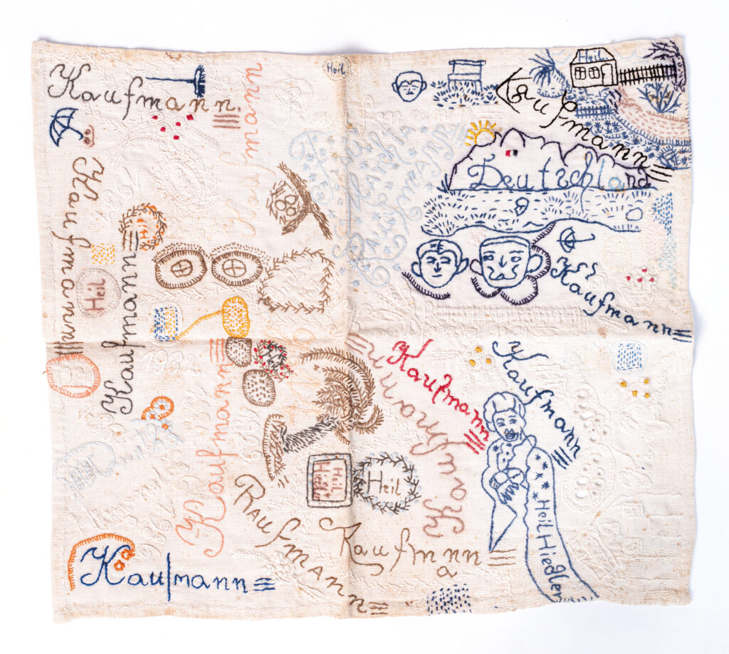 Das Taschentuch ist nahezu quadratisch. Mit blauem, braunem, schwarzem, weißem und rotem Faden sind die Schriftzüge und Motive gestickt. Die Motive sind durcheinander gestickt und überlagern sich teilweise.