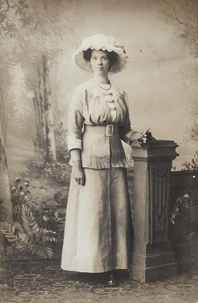Es sind drei schwarz-weiße Bilder nebeneinander. Zwei rechteckige und in der Mitte ein ovales Porträtbild. Das linke Bild zeigt Therese Schubert in einem hellen opulenten Kleid mit hellem Hut. Sie steht sehr aufrecht und hat die rechte Hand hinter dem Rücken. Das mittlere ist ein Porträt. Therese Schubert trägt ein dunkles Oberteil mit einem hellen Überwurf. Ihre Haare sind locker nach hinten gesteckt. Sie blickt freundlich direkt in die Kamera. Das rechte Bild zeigt Therese Schubert in einem hellen opulenten Kleid mit hellem Hut. Sie steht an eine Säule gelehnt. Sie blickt freundlich direkt in die Kamera.