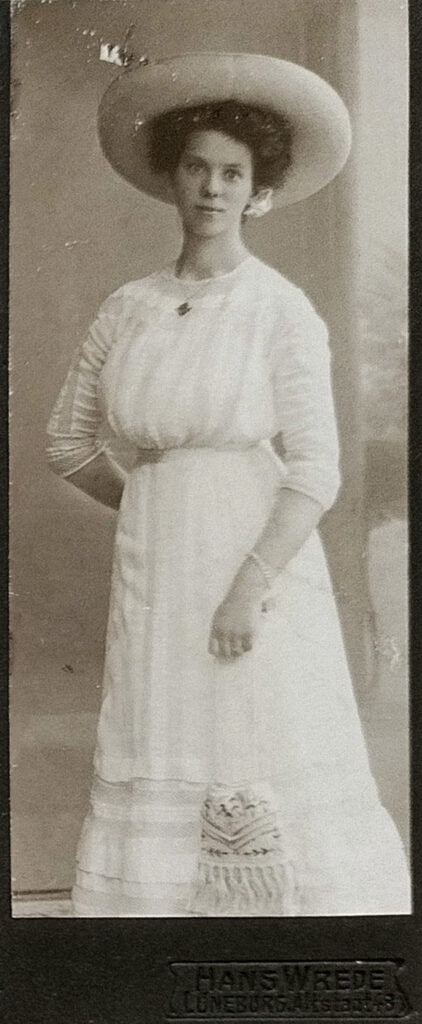 Es sind drei schwarz-weiße Bilder nebeneinander. Zwei rechteckige und in der Mitte ein ovales Porträtbild. Das linke Bild zeigt Therese Schubert in einem hellen opulenten Kleid mit hellem Hut. Sie steht sehr aufrecht und hat die rechte Hand hinter dem Rücken. Das mittlere ist ein Porträt. Therese Schubert trägt ein dunkles Oberteil mit einem hellen Überwurf. Ihre Haare sind locker nach hinten gesteckt. Sie blickt freundlich direkt in die Kamera. Das rechte Bild zeigt Therese Schubert in einem hellen opulenten Kleid mit hellem Hut. Sie steht an eine Säule gelehnt. Sie blickt freundlich direkt in die Kamera.
