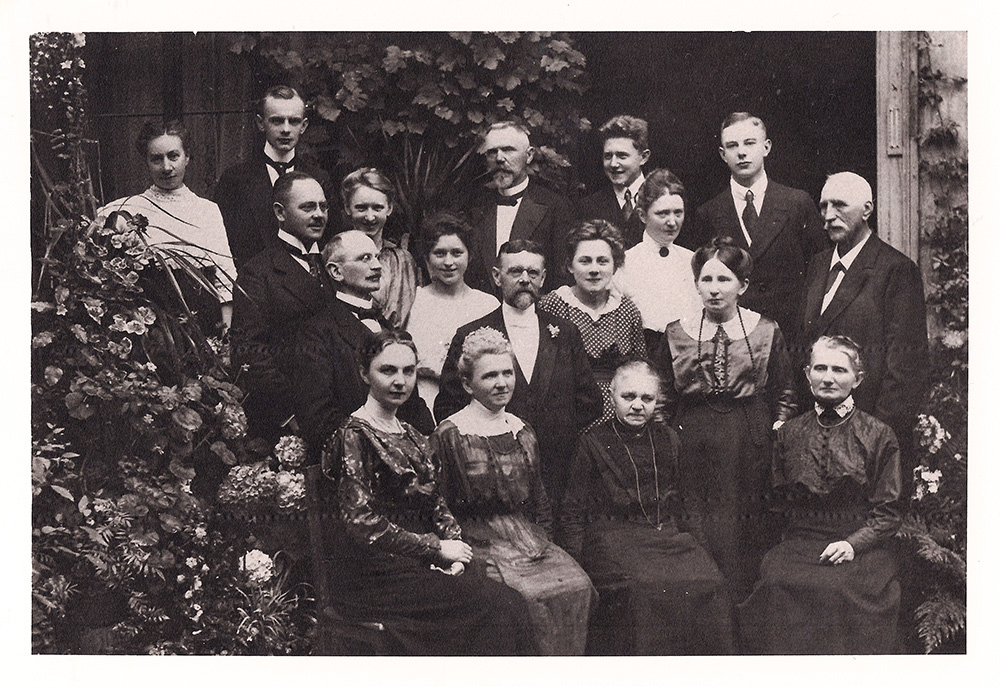 Es ist ein schwarz-weißes Gruppenfoto der Familie Biester. Zwischen Blumen und Pflanzen stehen 18 Personen. Sie sind unterschiedlich alt. Alle Männer tragen Anzug mit Krawatte oder Fliege. Die Frauen tragen schmuckvolle Kleider. Heinrich Biester hat die Haare kurzgeschnitten und streng zurückgekämmt. Er blickt ernst in die Kamera.