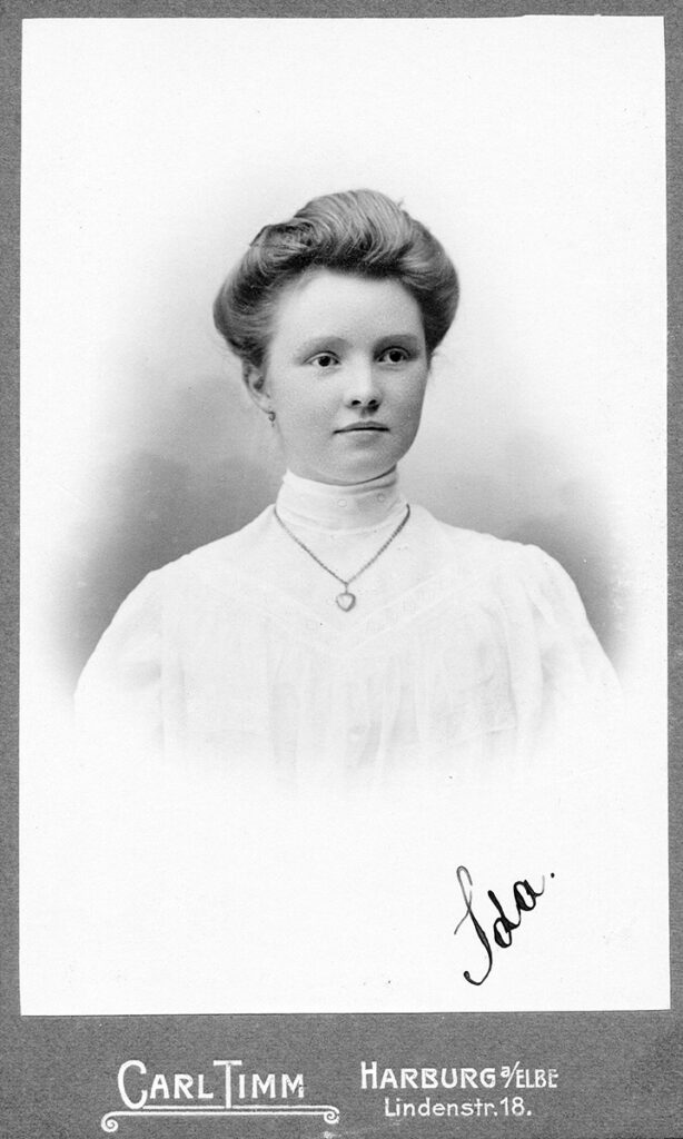 Das schwarz-weiße Porträtfoto ist auf dem Papier eines Fotografen gedruckt. Ida Zettel trägt ein helles hochgeschlossenes Kleid. Sie hat die Haare voluminös nach hinten gesteckt. Sie blickt freundlich leicht an der Kamera vorbei. Sie trägt eine Kette mit Herzanhänger.