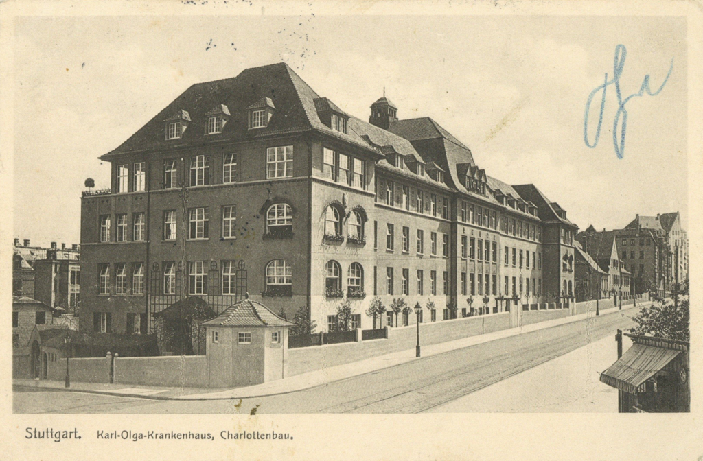 It is a black and white drawing of the house. It has four storeys and an extended roof with small dormers. The house is plastered and has mullioned windows. At the corner of the building, the windows are round at the top. It is surrounded by a plastered wall. There is a room with small windows in the wall at the corner of the street.