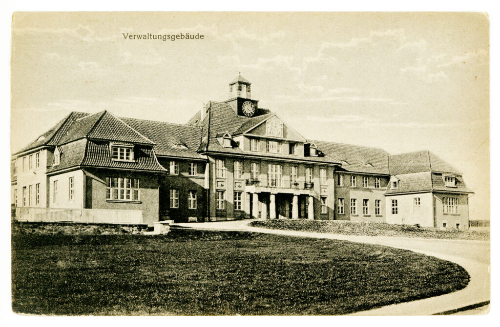 Die vergilbte Postkarte zeigt das Verwaltungsgebäude von Pfafferode. Das Gebäude hat ein zentrales Eingangshaus und davon abgehend zu jeder Seite einen Flügel mit Vorbau. Das Gebäude ist im Hauptportal zweistöckig mit einer Turmuhr auf dem Dach. Die Seitenflügel des Gebäudes sind einstöckig, wobei das Dachgeschoss Gauben hat und vermutlich auch genutzt wird. Das Gebäude ist verputzt und hat helle Sprossenfenster.