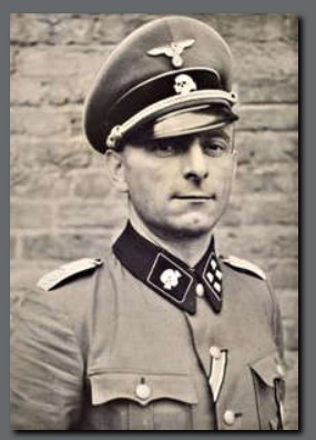 Es ist ein schwarz-weißes Porträtfoto von Kurt Eimann. Er trägt eine SS-Uniform mit dem Totenkopf-Emblem am Kragen und an der Schirmmütze. Kurt Eimann steht leicht seitlich zur Kamera. Er blickt mit festem Blick direkt in die Kamera. Seine Uniformmütze sitzt leicht schief auf dem Kopf. An seiner Uniform prangt ein Orden.