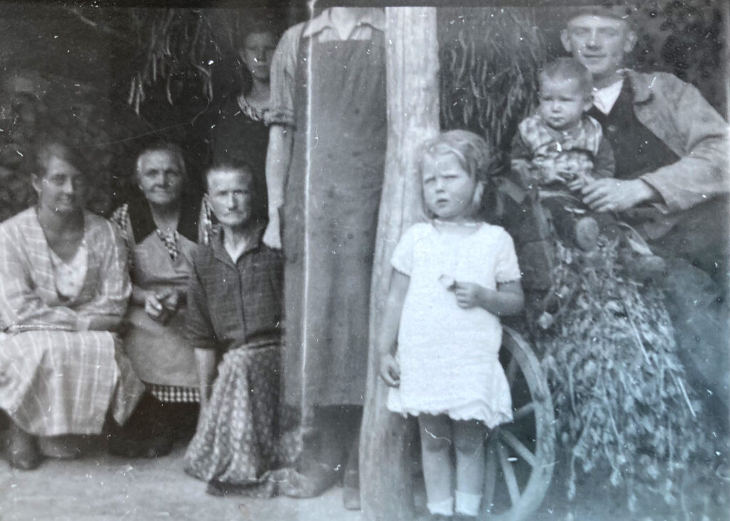 Es ist ein leicht verschwommenes, etwas zerkratztes schwarz-weißes Foto. Zu sehen sind acht Personen in landwirtschaftlicher Kleidung. Rechts sitzt Wilhelm Eilers mit seinem Sohn und Tochter. Rechts daneben hocken drei Frauen für das Foto. Dazwischen steht eine Person in groben Holzschuhen und Schürze. Ihr Kopf ist nicht mit auf dem Bild. Alle blicken ernst in die Kamera.