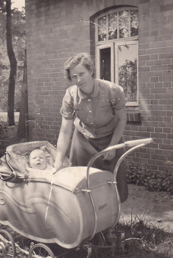 Es ist ein schwarz-weißes Foto. Vor einem Haus ist ein großer Kinderwagen. Fritz Wehde schaut mit interessiertem Blick zur Kamera. Tante Wilma steht hinter dem Wagen und hat eine Hand bei Fritz. Sie trägt eine kurzärmelige Bluse mit Rock. Sie blickt in die Kamera.