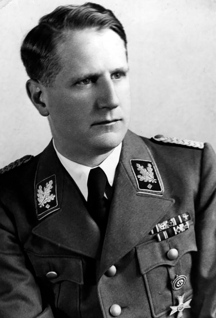Das ist ein schwarz-weißes Porträtfoto von Leonard Conti. Er trägt eine Uniform. Er trägt Abzeichen und Orden. Er blickt mit ernstem Blick rechts aus dem Bild heraus. Sein Haar ist zurückgekämmt und sein Körper leicht nach links geneigt.