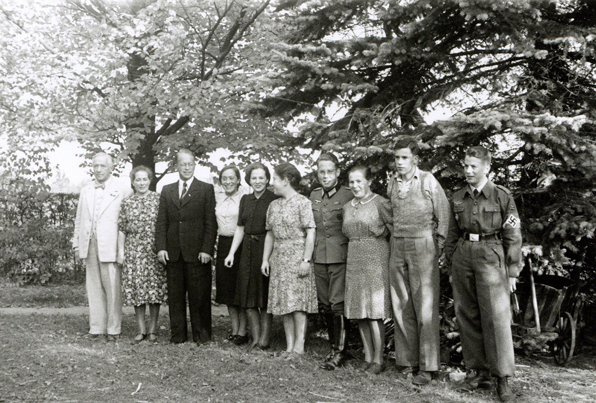 Es ist ein schwarz-weißes Gruppenfoto. Die Familie Redepenning steht aufgereiht auf einer Wiese vor Bäumen im Park. Ganz links steht Rudolf Redepenning. Er trägt einen hellen Anzug. Neben ihm steht seine Frau in einem geblümten Kleid, die Haare hochgesteckt. Es reihen sich nach rechts die acht erwachsenen Kinder: vier Söhne und vier Töchter. Drei Söhnen tragen eine Uniform. Die Töchter tragen Kleider bzw. Rock und Bluse. Es ist ein warmer Herbsttag, die Sonne scheint.