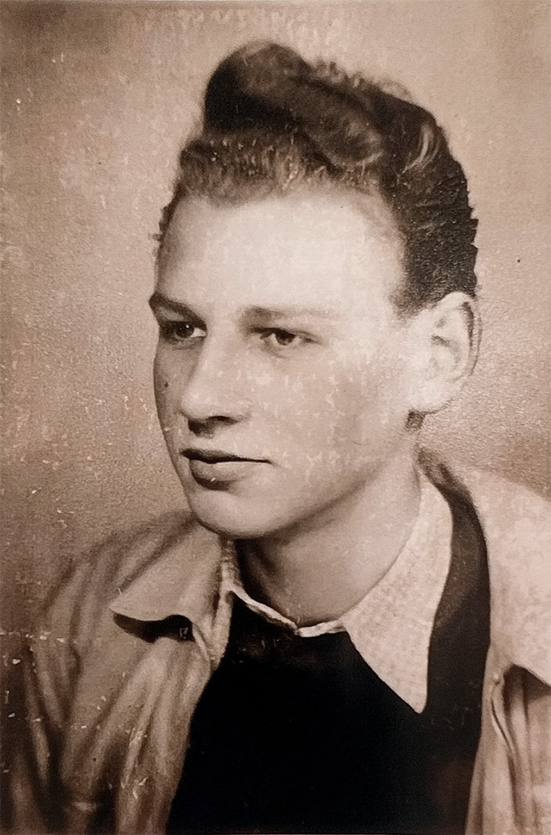Das Foto ist sepiafarben. Ernst Daps Junior ist bis zur Brust zu sehen. Er trägt eine helle Jacke, einen dunklen Pullover und darunter ein Hemd. Seine Haare sind zu einer Tolle frisiert. Er blickt nach links.