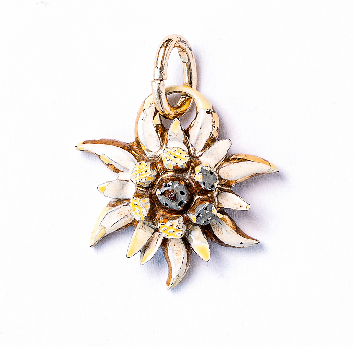 Die Edelweißblüte ist aus Metall gearbeitet. Sie ist weiß, gelb und schwarz emailliert. Sie hat einen ovalen Anhänger.