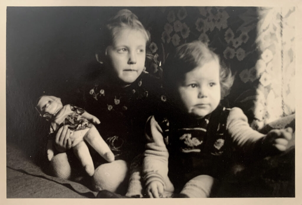 Es ist ein schwarz-weißes Foto. Die beiden Geschwister sitzen eng beieinander. Sonja hält eine Puppe im Arm. Die beiden blicken nach rechts.
