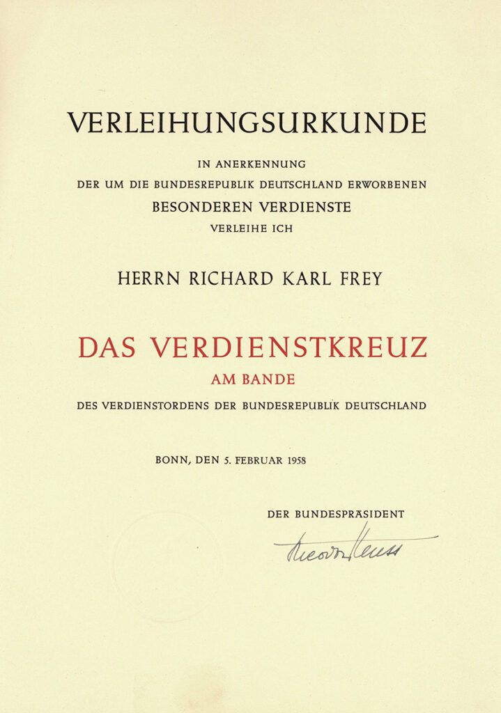 In der Vitrine liegt die Urkunde. Sie ist auf gelbes Papier gedruckt. Der Name des Ordens ist rot und groß geschrieben. Die Urkunde ist vom Bundespräsidenten unterschrieben.