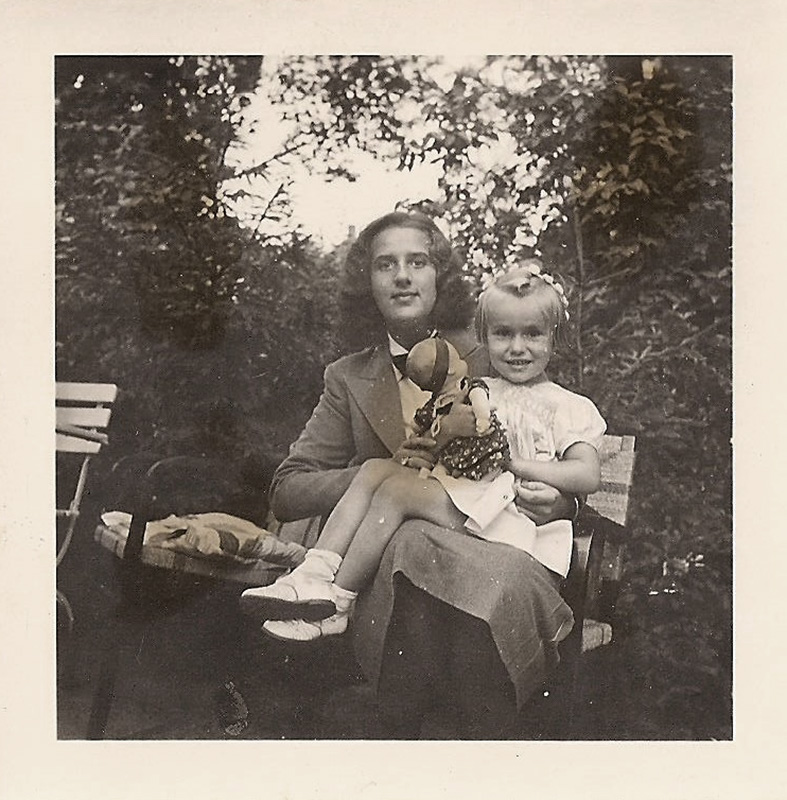 Es ist ein schwarz-weiß Foto. Es zeigt die Mutter sitzend mit der Cousine auf dem Schoß. Sie sitzen in einem Garten. Beide tragen schicke Kleidung und wirken sehr vergnügt.
