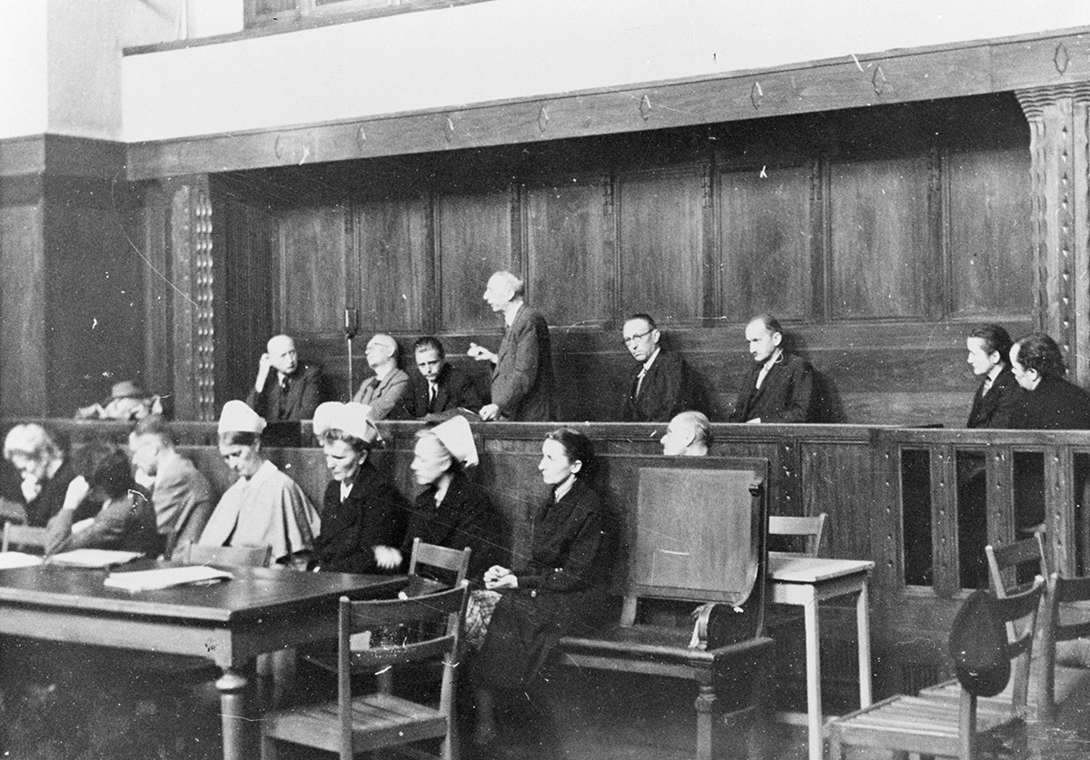 Es ist ein schwarz-weißes Foto. In drei Reihen sitzen Personen auf erhöhten Holzbänken. Die Bänke sind durch Tische und Balustraden voneinander getrennt. Die Männer tragen Anzüge. Einige der Frauen tragen weiße Schwesternhauben.