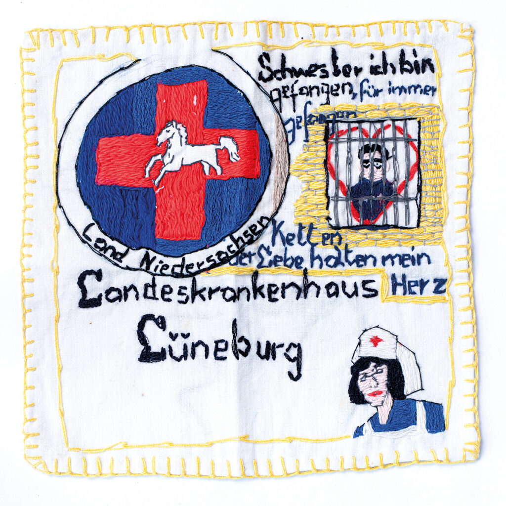 Auf hellem Stoff ist eine gelbe Umrandung gestickt. Oben links findet sich ein rotes Kreuz vor blauem Hintergrund mit einem weißen Pferd in der Mitte. Unten rechts eine Person in Schwesternkleidung. Dazu der Schriftzug: Oben rechts eine skizzierte Person mit Herz hinter Gittern. Dazu der Schriftzug: »Schwester ich bin gefangen für immer gefangen« sowie »Ketten der Liebe halten mein Herz«.