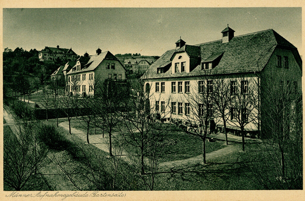 It is a black and white photo. It is slightly yellowed. It is labelled at the bottom. It shows two similar two-storey buildings with dormer windows. Both buildings are surrounded by hedges and trees. The buildings are light in colour and have a dark roof with two small towers on the ridge. They have many mullioned windows on the floors and a curved gate entrance on the left-hand side.