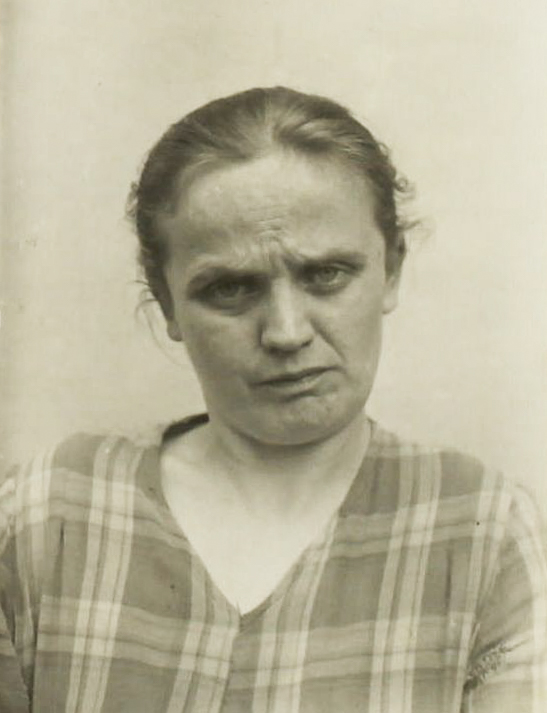 Es ist ein schwarz-weißes Porträtfoto. Olga Schulze trägt eine karierte Bluse. Sie hält den Kopf leicht schräg und guckt zur Kamera. Ihr Blick wirkt skeptisch.
