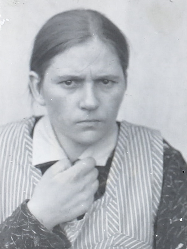 Es ist ein schwarz-weißes Porträtfoto. Else Böhling trägt einen gestreiften Kittel mit einer dunklen Bluse mit Kragen. Ihr Haar ist hinten zusammengebunden. Sie blickt in die Kamera. Ihr Blick wirkt skeptisch.