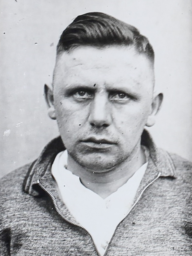 Es ist ein schwarz-weißes Porträtfoto. August Böhling trägt ein helles T-Shirt mit Pullover darüber. Sein Haar ist über der Stirn nach oben frisiert. Er guckt in die Kamera.