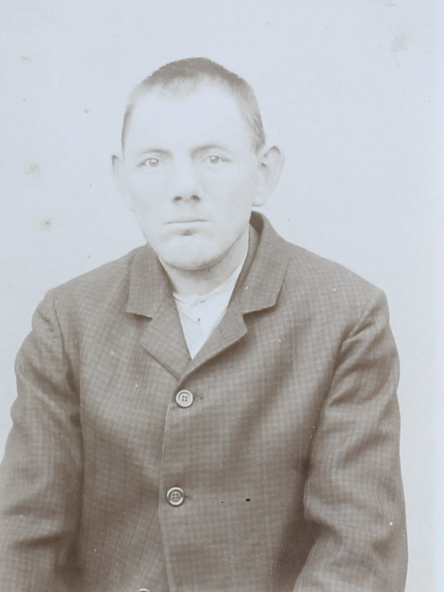 Es ist ein schwarz-weißes Porträtfoto. Es ist sehr hell. Wilhelm Hosse trägt eine dunkle geknöpfte Jacke. Sein Haar ist kurz geschoren. Er guckt mit ernstem Blick in die Kamera.