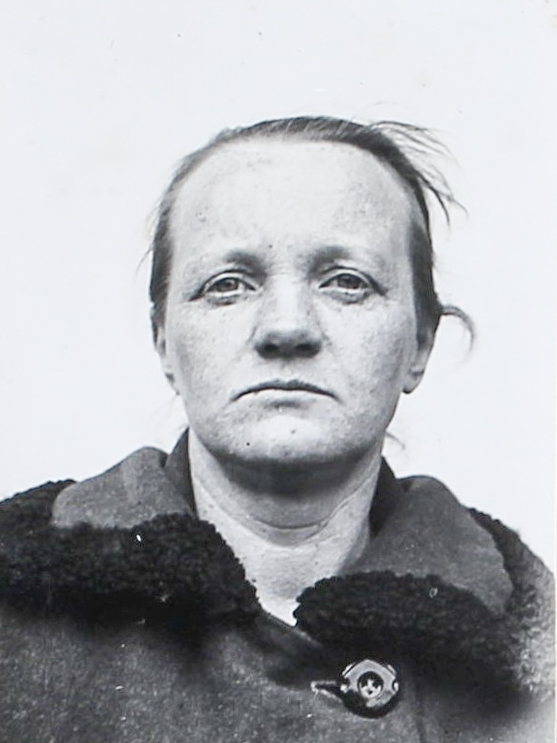 Es ist ein schwarz-weißes Porträtfoto. Elly Schack trägt eine dunkle Jacke. Ihr Haar ist hinten zusammengebunden. Einige Strähnen stehen heraus. Sie blickt direkt in die Kamera. Ihre Augen sind zusammengekniffen.