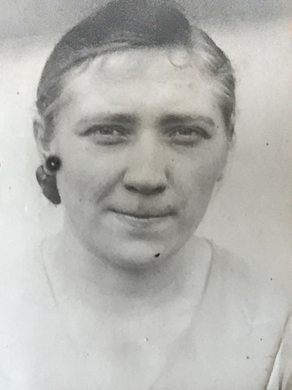 Es ist ein schwarz-weißes Porträtfoto. Dora Schulz trägt ein helles Oberteil. Ihr Haar ist nach hinten frisiert. Sie hat den Mund zusammengekniffen und guckt in die Kamera.