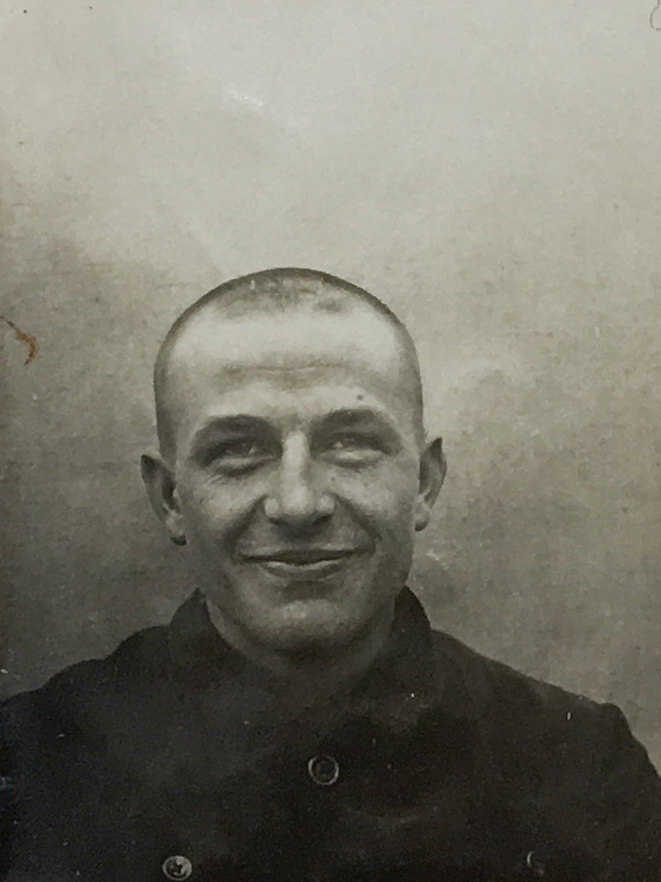 Es ist ein schwarz-weißes Porträtfoto. Es ist sehr dunkel. Hermann Brüggemann trägt eine dunkle Jacke. Sein Haar ist kurz geschoren. Er guckt freundlich in die Kamera.