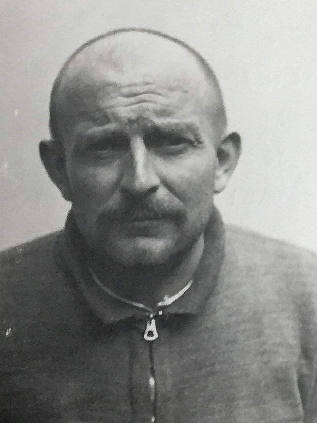Es ist ein schwarz-weißes Porträtfoto. Heinrich Schwammberger trägt einen hochgeschlossenen Troyer. Sein Haar ist kurz geschoren. Er trägt einen Oberlippenbart. Er guckt in die Kamera.