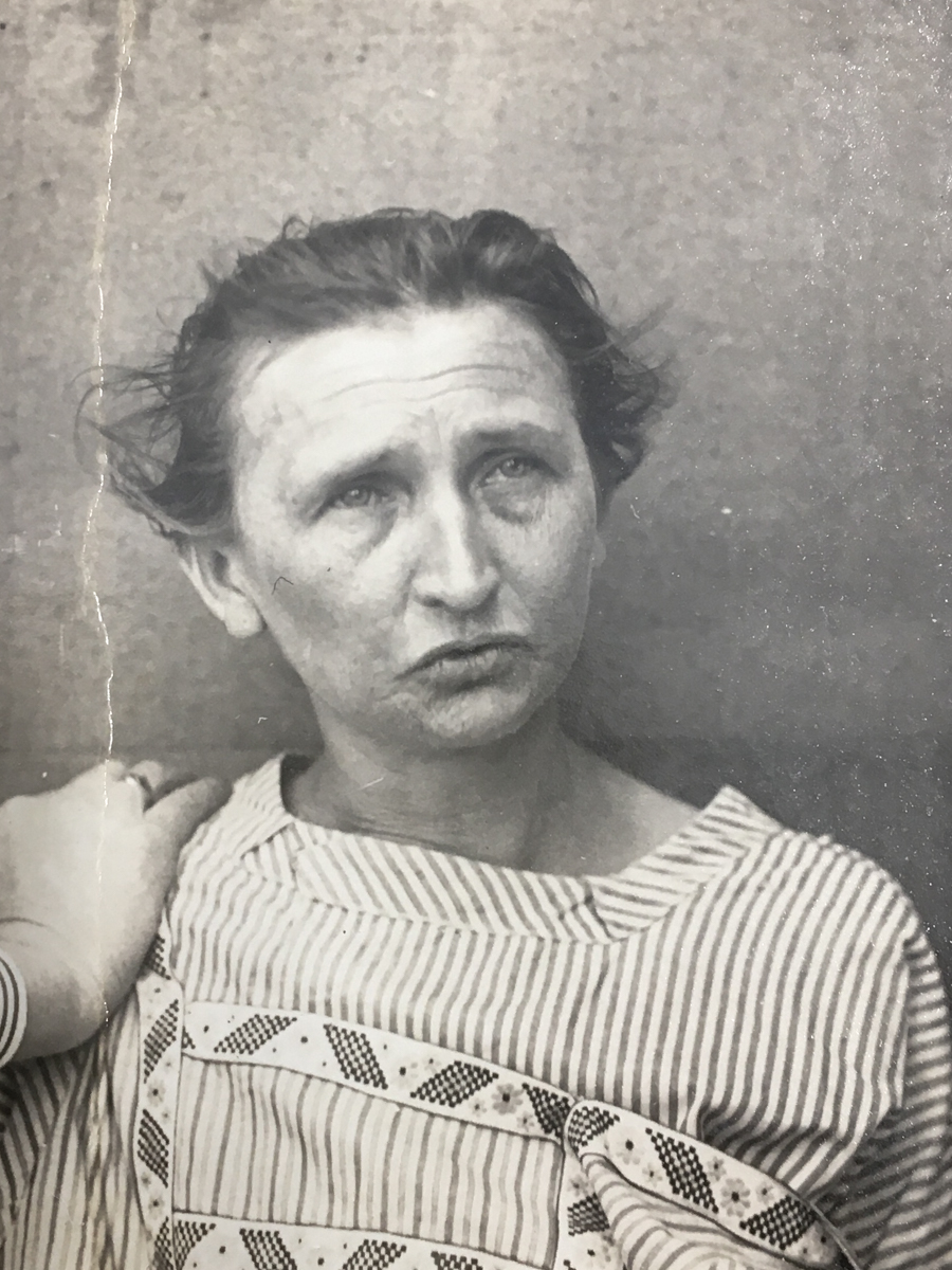 Es ist ein schwarz-weißes Porträtfoto. Anna Schwarz trägt ein gestreiftes Hemd. Die Haare sind nach hinten gebunden und stehen leicht ab. Sie blickt mit leicht geöffnetem Mund nach oben rechts. An ihrer Schulter ist die Hand einer anderen Person zu sehen, die sie an die Wand hinter ihr drückt.