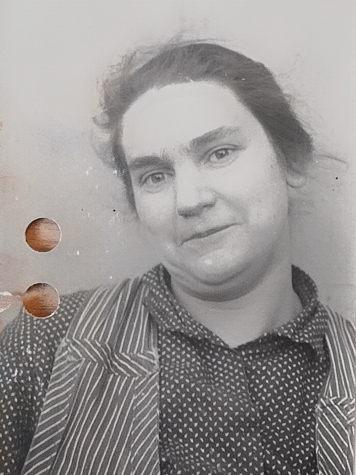 Es ist ein schwarz-weißes Porträtfoto. Anna Schwarz trägt ein gestreiftes Hemd. Die Haare sind nach hinten gebunden und stehen leicht ab. Sie blickt mit leicht geöffnetem Mund nach oben rechts. An ihrer Schulter ist die Hand einer anderen Person zu sehen, die sie an die Wand hinter ihr drückt.