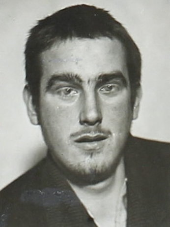 Es ist ein schwarz-weißes Porträtfoto. Gerhard Glass trägt ein dunkles Hemd. Die Haare sind kurz geschnitten und nach hinten gekämmt. Er blickt in die Kamera.