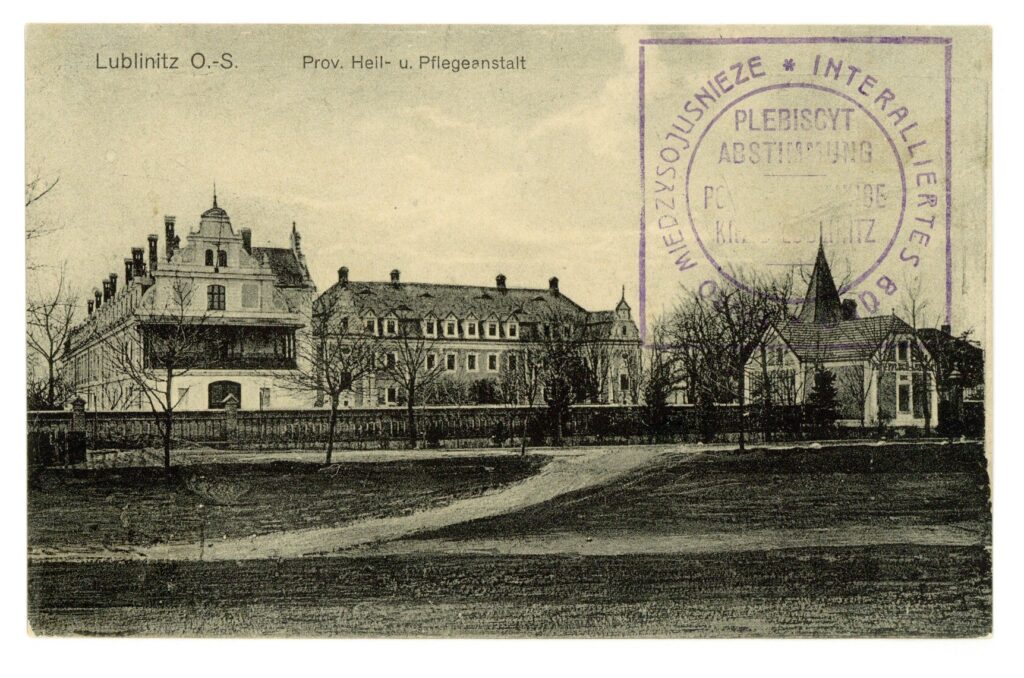 It is a black-and-white postcard. It shows the Loben sanatorium and nursing home from a distance. It is a charcoal drawing. Sand paths lead to the walled institution. Three buildings are visible. The postcard has been stamped with a postmark in Polish.